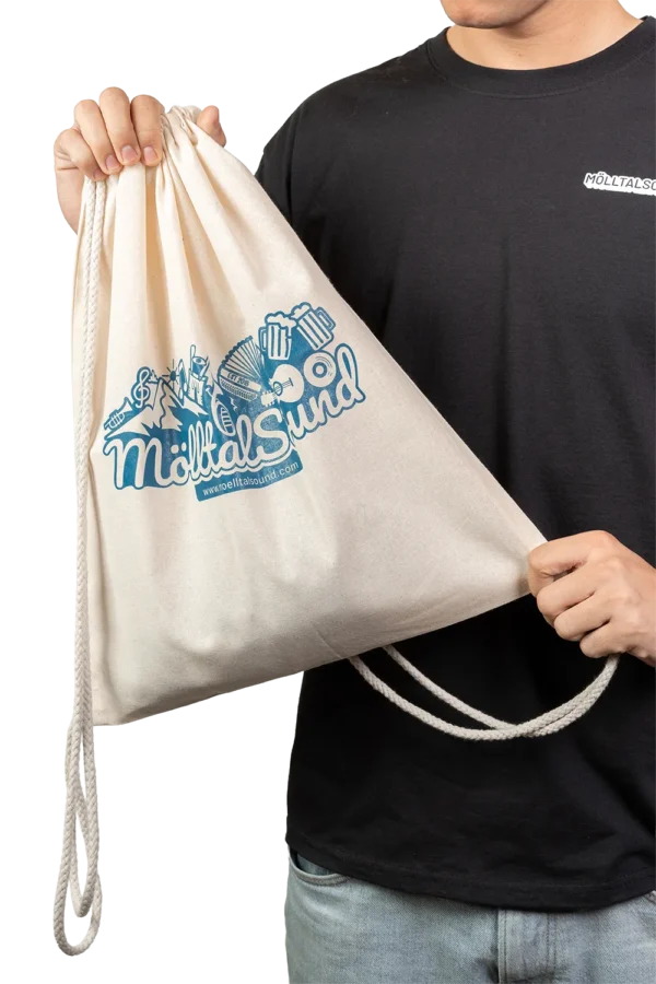 Person hält einen naturfarbenen MölltalSound-Turnbeutel mit großem blauem Logo und Illustration auf der Vorderseite.