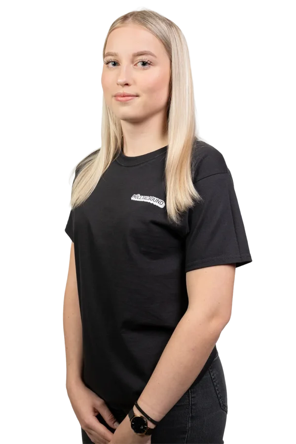 Junge Frau im schwarzen „Vibe“-T-Shirt von MölltalSound, seitlich stehend, mit kleinem Frontlogo auf der linken Brust.